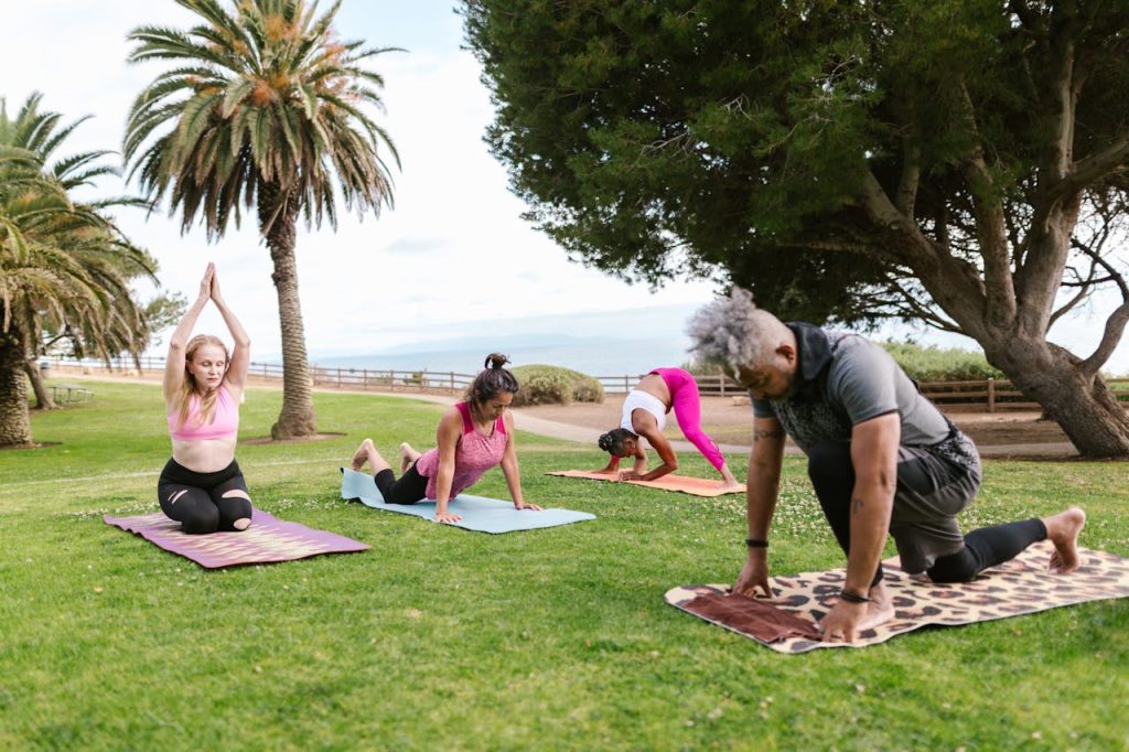nature-love-relaxation-trees-8172904 Diverse group practicing yoga outdoors in a sunny park setting. Emphasizes fitness and wellness.
